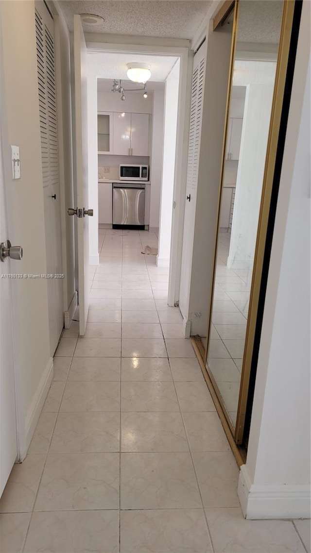 corridor featuring light tile patterned floors, baseboards, and a textured ceiling