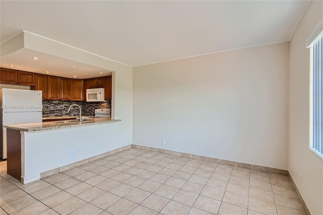 kitchen with backsplash, light stone counters, a peninsula, white appliances, and a sink