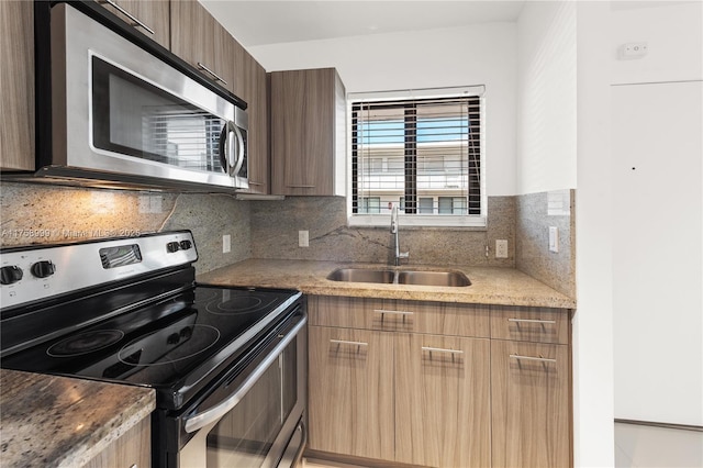 kitchen with light stone counters, a sink, appliances with stainless steel finishes, modern cabinets, and backsplash