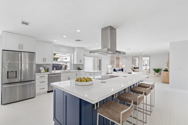 kitchen featuring light stone counters, a sink, decorative backsplash, appliances with stainless steel finishes, and island range hood