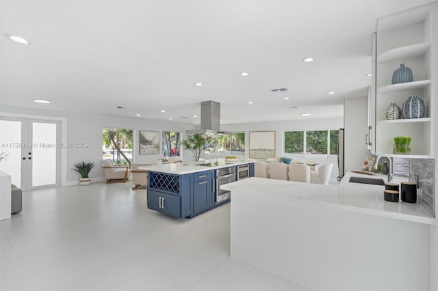 kitchen with open shelves, island exhaust hood, a sink, stainless steel oven, and blue cabinets