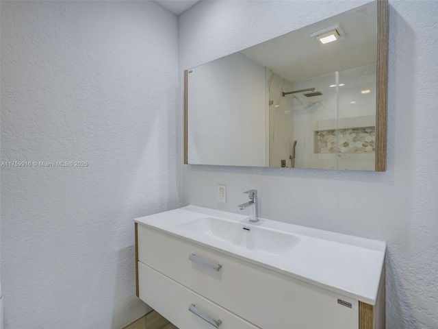 full bath with vanity, a walk in shower, and a textured wall