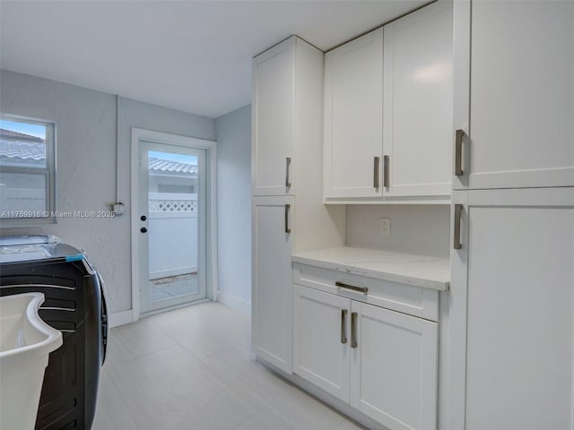 kitchen with washer and dryer, baseboards, light stone counters, and white cabinets