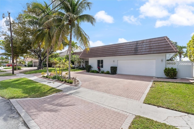 view of front of home featuring mansard roof, decorative driveway, a garage, and stucco siding