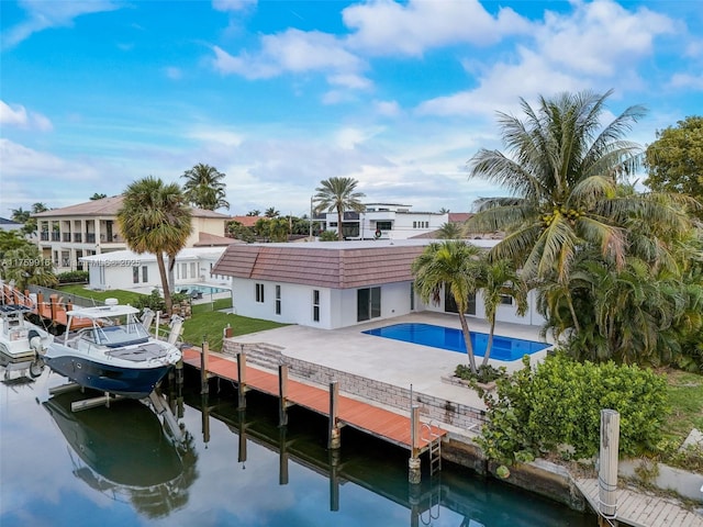 back of house featuring a water view, a tiled roof, stucco siding, an outdoor pool, and a patio