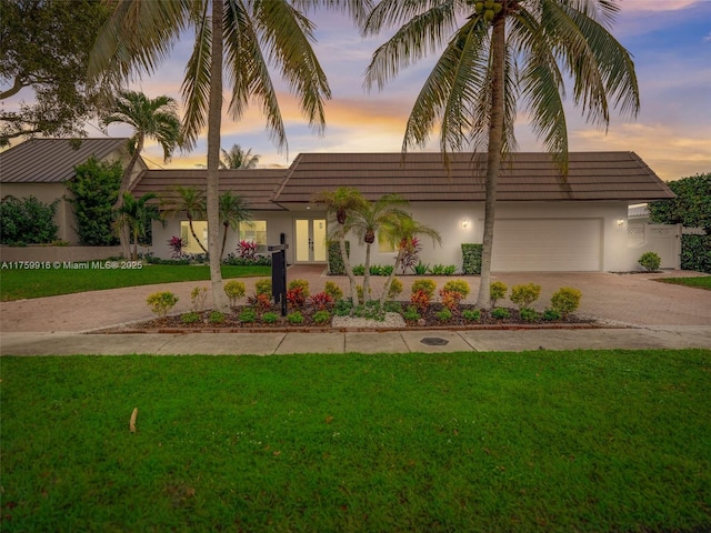 view of front facade with a garage, stucco siding, decorative driveway, and a yard