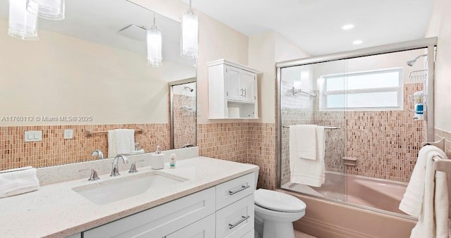 bathroom with vanity, a wainscoted wall, shower / bath combination with glass door, tile walls, and toilet