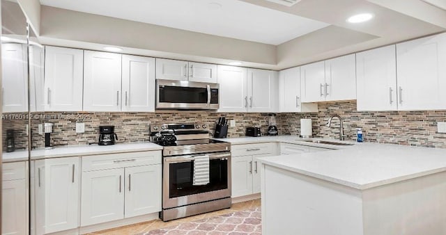 kitchen with light countertops, decorative backsplash, appliances with stainless steel finishes, white cabinets, and a sink