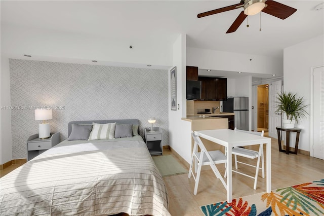 bedroom featuring an accent wall, baseboards, freestanding refrigerator, and wallpapered walls