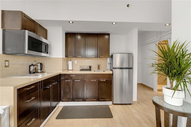 kitchen with a sink, light countertops, dark brown cabinets, appliances with stainless steel finishes, and tasteful backsplash