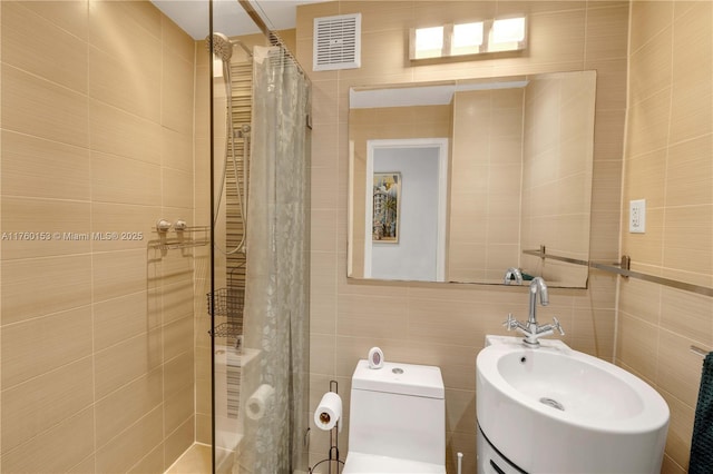 full bath with visible vents, toilet, a sink, tile walls, and tiled shower