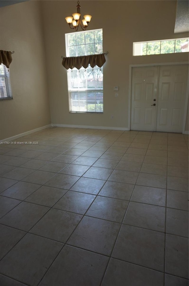 tiled entryway with a chandelier, baseboards, and a towering ceiling