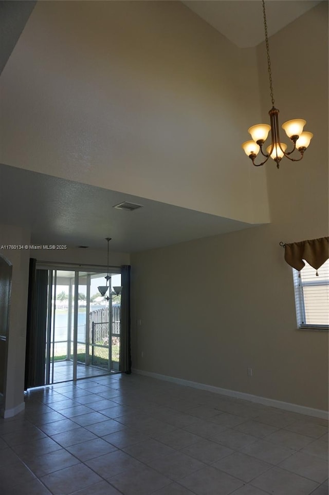 empty room with baseboards, visible vents, an inviting chandelier, a high ceiling, and tile patterned flooring