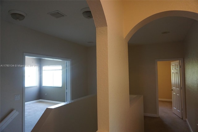 hall with carpet, visible vents, baseboards, arched walkways, and a textured wall