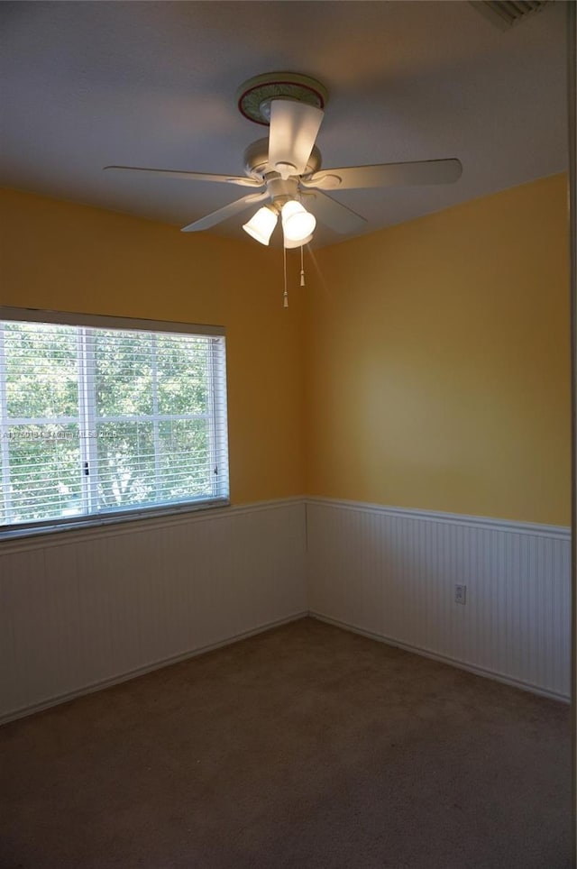 empty room featuring a wainscoted wall, ceiling fan, and carpet floors