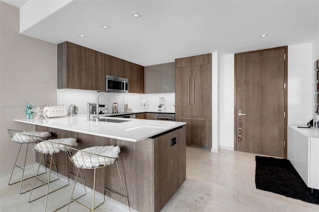 68 SE 6th St Unit 1404, Miami, FL 33131 - kitchen featuring a breakfast bar, a peninsula, a sink, stainless steel microwave, and modern cabinets