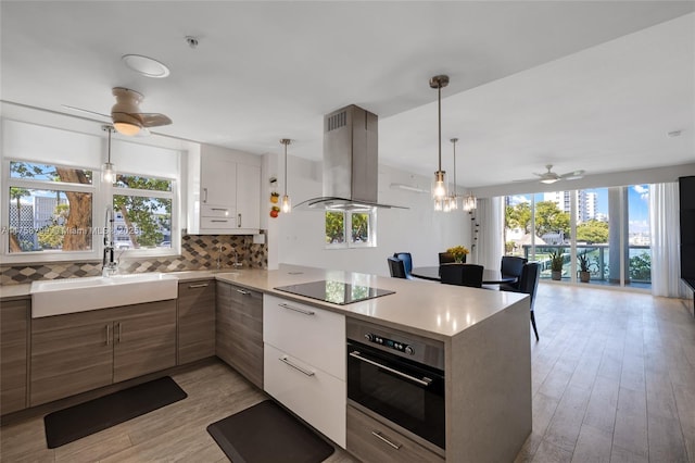 kitchen with a peninsula, decorative backsplash, wall oven, black electric stovetop, and exhaust hood