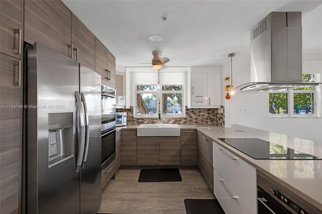 kitchen featuring a healthy amount of sunlight, a sink, stainless steel appliances, backsplash, and island range hood