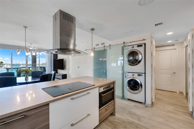 kitchen featuring island exhaust hood, light countertops, stacked washer and dryer, wall oven, and black electric stovetop