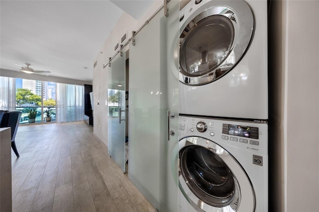 washroom featuring light wood-style flooring, stacked washing maching and dryer, a barn door, ceiling fan, and laundry area