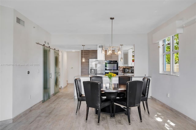 dining room featuring a barn door, light wood-style floors, visible vents, and a notable chandelier