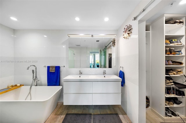 bathroom with a spacious closet, a freestanding bath, double vanity, wood finished floors, and a sink