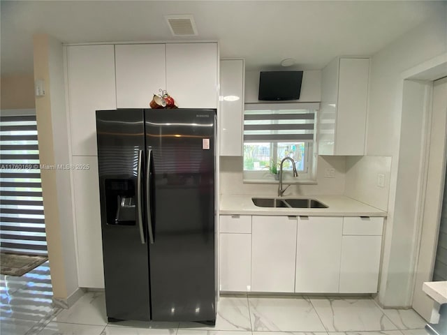 kitchen featuring visible vents, a sink, light countertops, marble finish floor, and black fridge