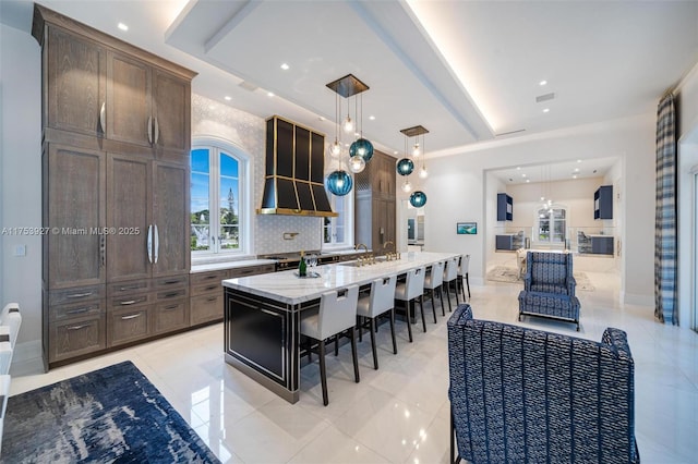 kitchen with light stone countertops, decorative light fixtures, a kitchen bar, decorative backsplash, and a large island with sink