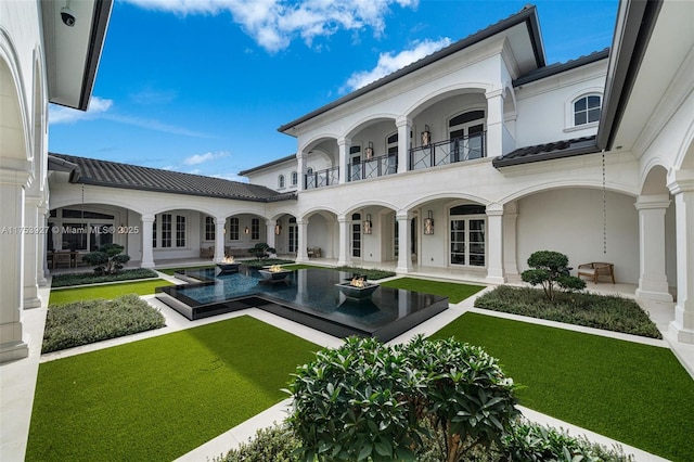 rear view of house featuring stucco siding, a patio, a lawn, and a balcony