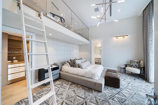 bedroom with ensuite bathroom, wood finished floors, a high ceiling, baseboards, and an accent wall