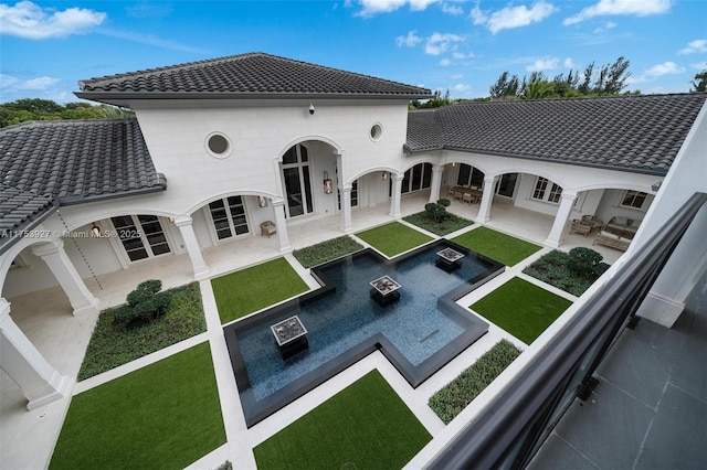 back of house featuring a patio area, a lawn, a tiled roof, and an outdoor fire pit