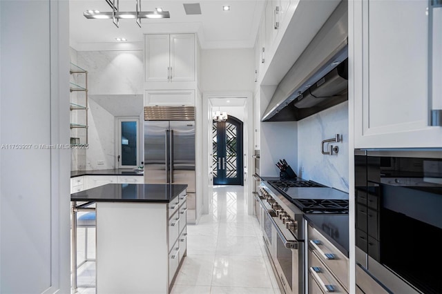 kitchen featuring dark countertops, a kitchen island, under cabinet range hood, premium appliances, and white cabinets