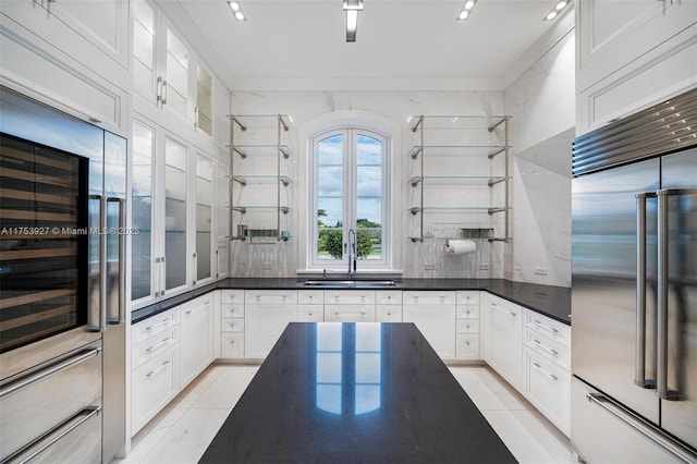 kitchen with a sink, stainless steel built in fridge, dark countertops, and light tile patterned floors