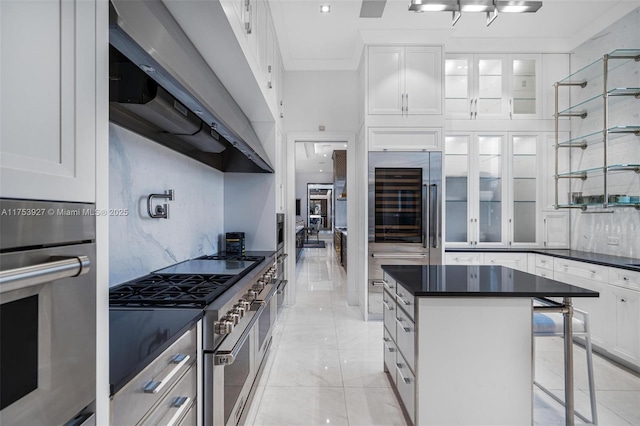 kitchen featuring dark countertops, appliances with stainless steel finishes, ventilation hood, and glass insert cabinets