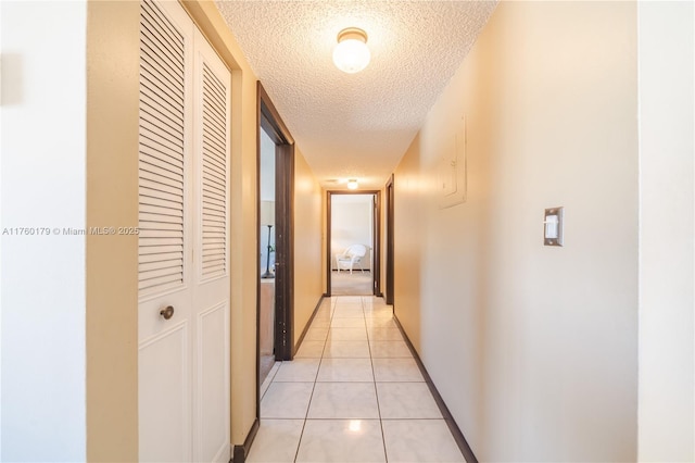 hall with light tile patterned flooring, baseboards, and a textured ceiling