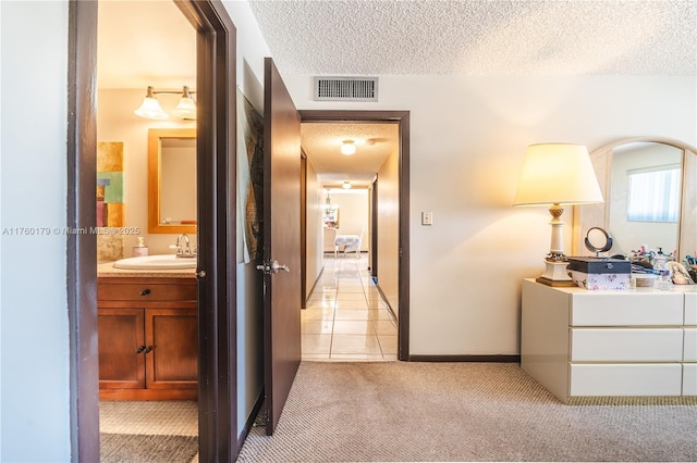 hall with visible vents, a sink, a textured ceiling, baseboards, and light colored carpet