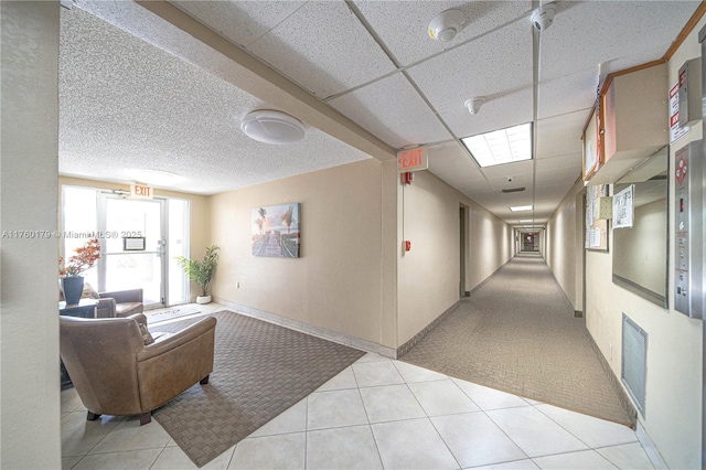 corridor featuring tile patterned floors, a drop ceiling, baseboards, and visible vents