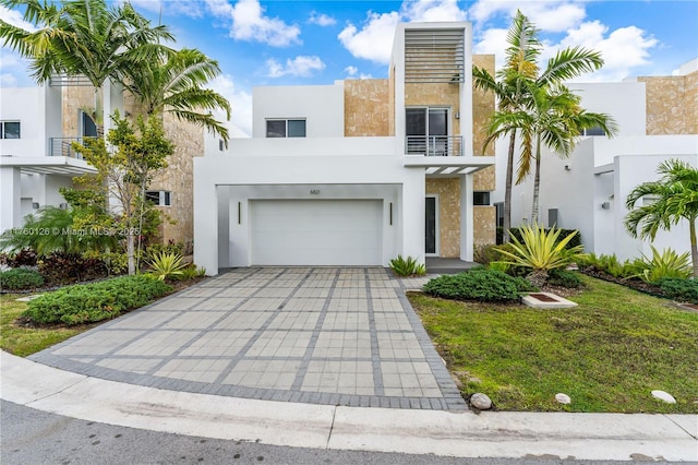 view of front of home featuring stucco siding, decorative driveway, a balcony, and a garage