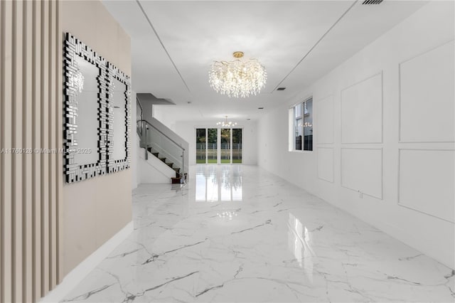 corridor featuring stairway, a notable chandelier, marble finish floor, and a decorative wall