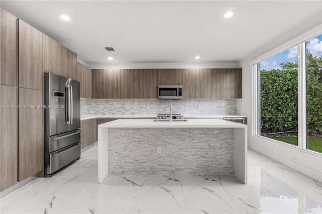 kitchen with modern cabinets, marble finish floor, backsplash, appliances with stainless steel finishes, and light countertops