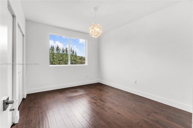 unfurnished bedroom with an inviting chandelier, dark wood-type flooring, and baseboards