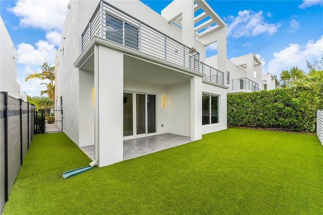 rear view of property with stucco siding, a lawn, fence, a balcony, and a patio area