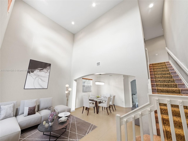 living area with visible vents, arched walkways, tile patterned flooring, a towering ceiling, and stairs