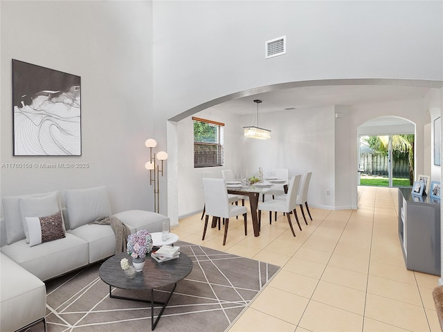 tiled living area featuring visible vents, arched walkways, baseboards, and a towering ceiling