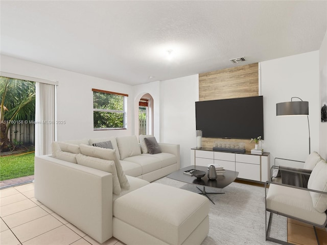 living area with light tile patterned floors, visible vents, arched walkways, and a textured ceiling