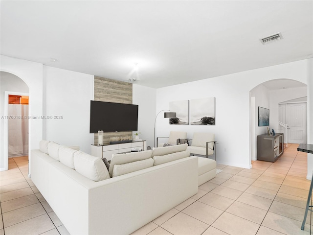 living area featuring light tile patterned flooring, visible vents, and arched walkways