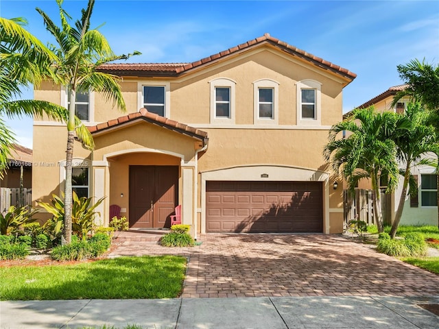 mediterranean / spanish-style home featuring decorative driveway, a tile roof, an attached garage, and stucco siding