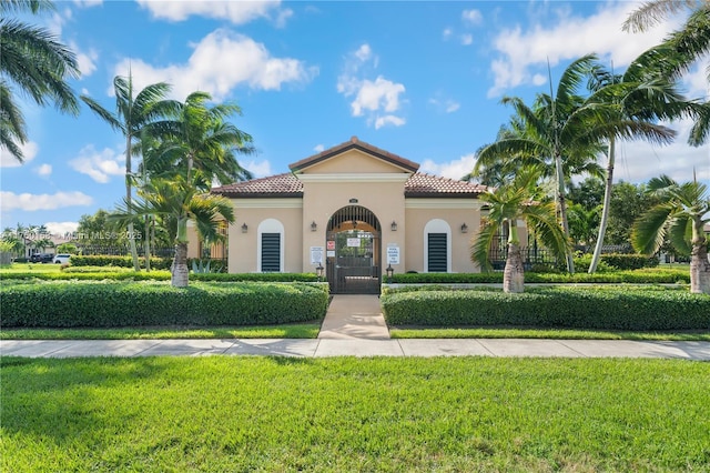 mediterranean / spanish home featuring a front lawn, a gate, a tile roof, and stucco siding