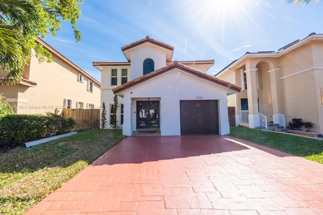 mediterranean / spanish house featuring fence, a tiled roof, stucco siding, decorative driveway, and an attached garage