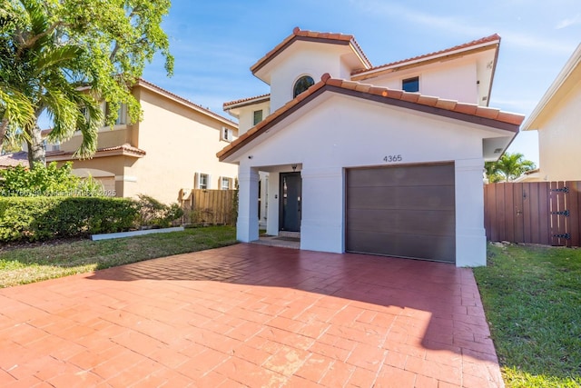 mediterranean / spanish house featuring decorative driveway, a garage, stucco siding, and fence